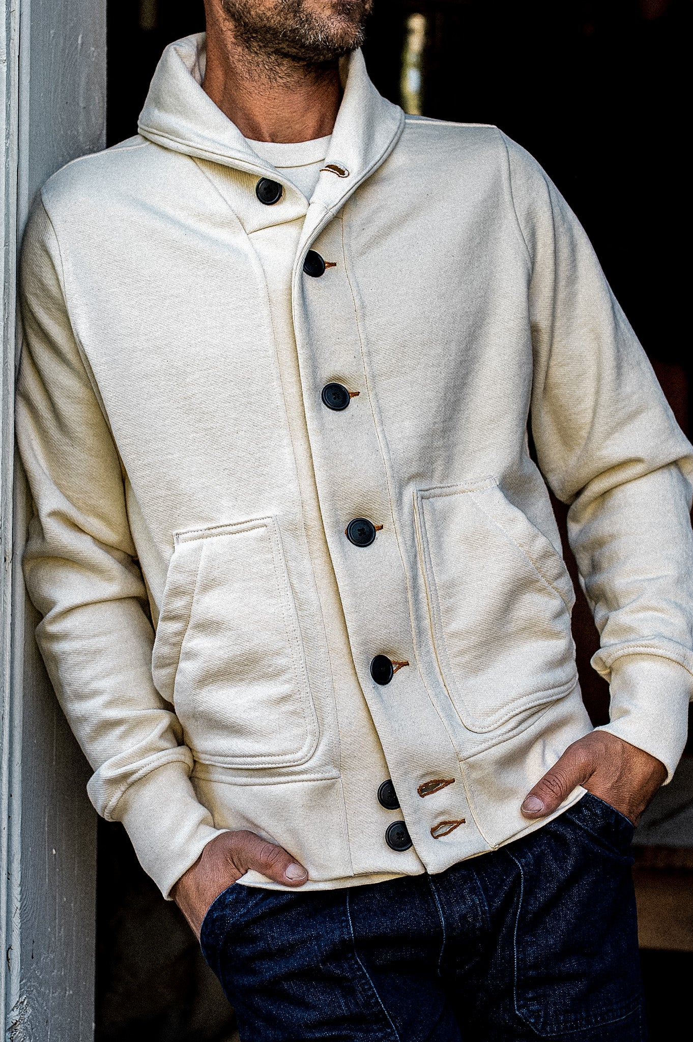 Man wearing natural French terry Bodega shawl cardigan with dark buttons over denim jeans.