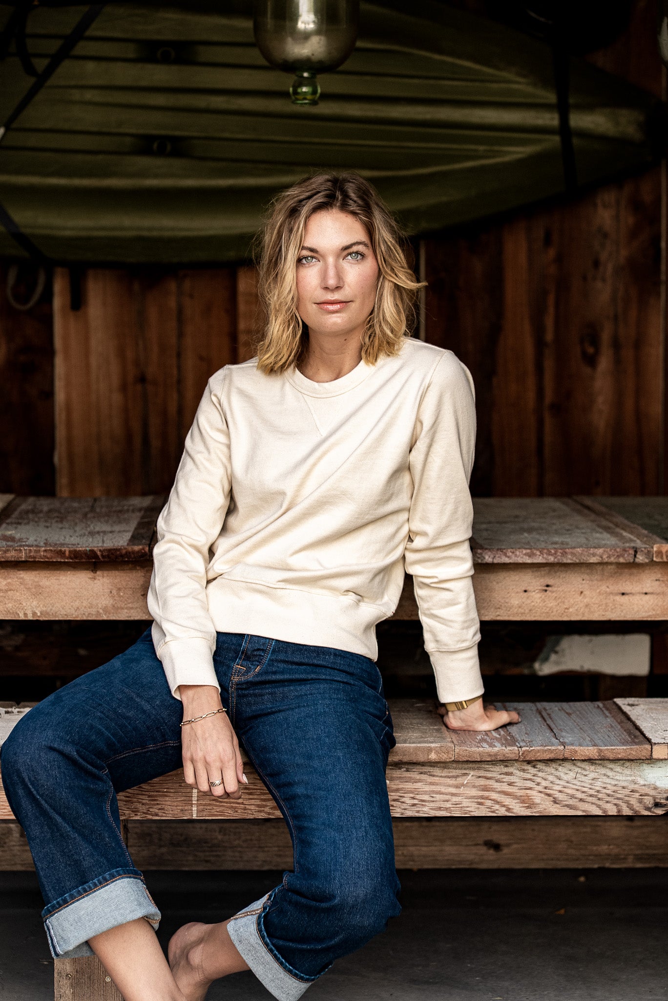 Woman wearing natural Stinson rugby jersey pullover with cuffed selvedge denim on a rustic bench.
