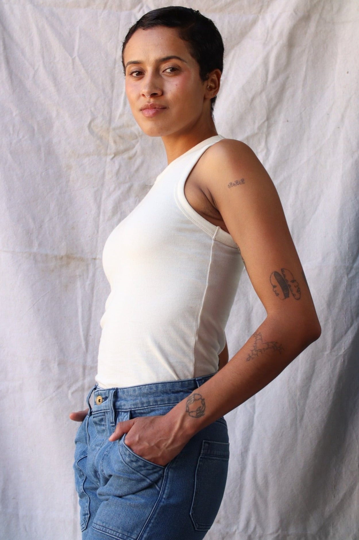 Side view of the natural cotton Bolinas tank tucked into blue jeans against a draped canvas backdrop.