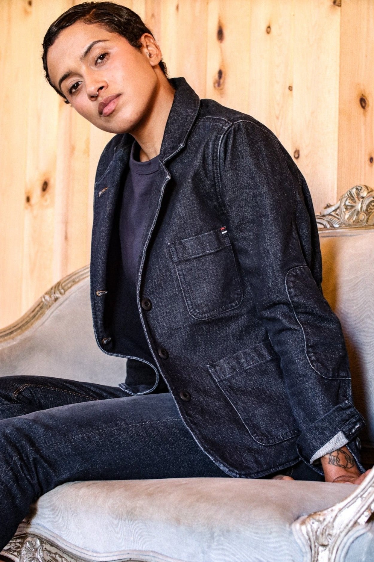 Person wearing dark indigo Scout denim chore blazer, seated on a vintage settee.