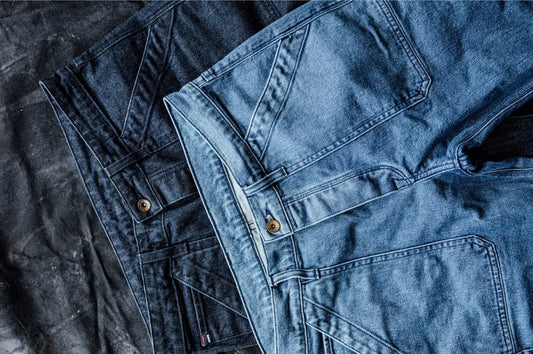 Ocean wash jeans in light and dark blue shades folded side-by-side on a textured black fabric surface.