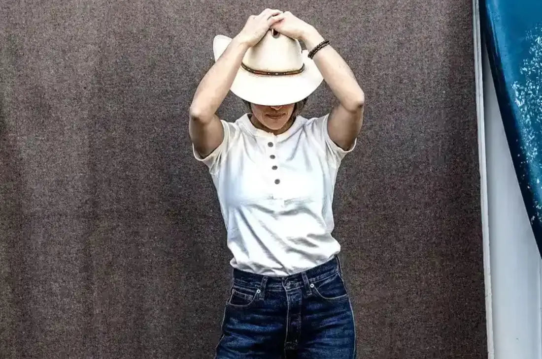 Jeans for casual wear paired with a white henley shirt and cowboy hat in a relaxed pose.