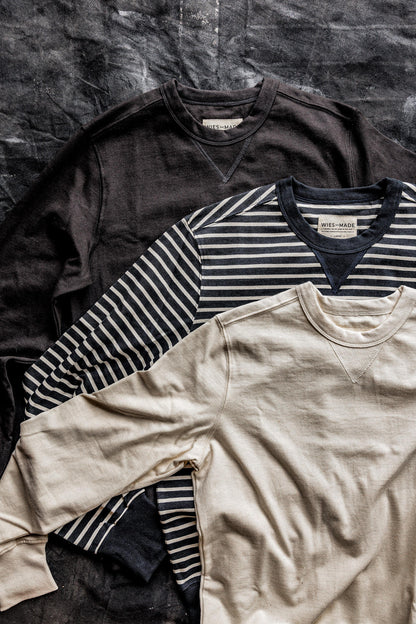 Three Stinson rugby jersey pullovers in basalt, navy stripe, and natural cream laid flat on a dark canvas.
