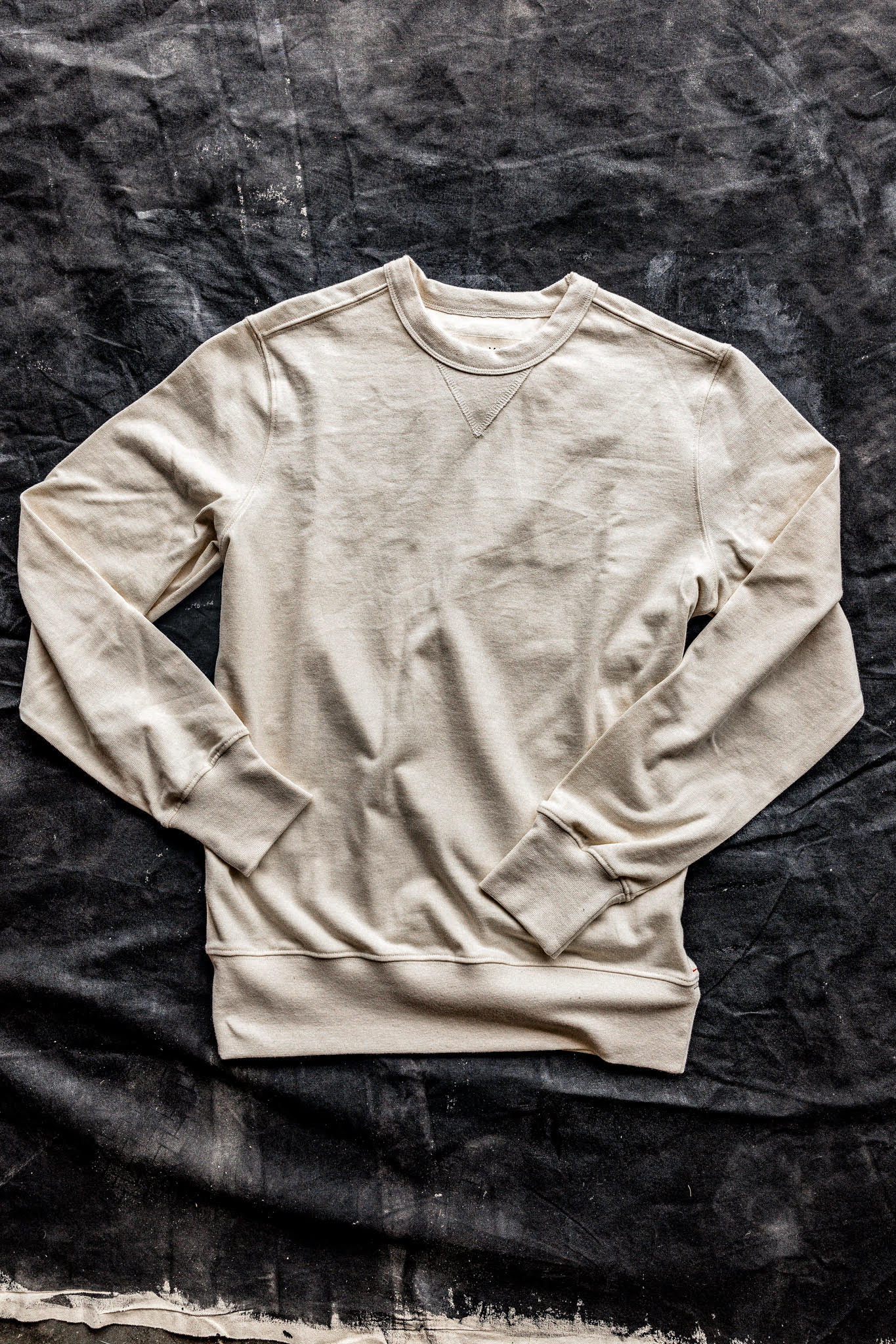 Natural cream cotton rugby jersey pullover laid flat on a dark canvas backdrop, showing crewneck and V-stitch detail.