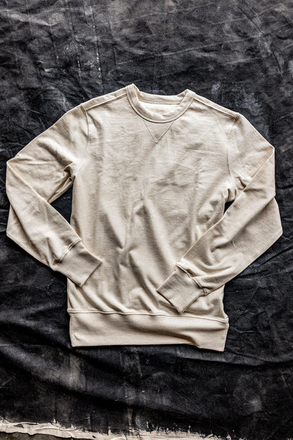 Natural cream cotton rugby jersey pullover laid flat on a dark canvas backdrop, showing crewneck and V-stitch detail.