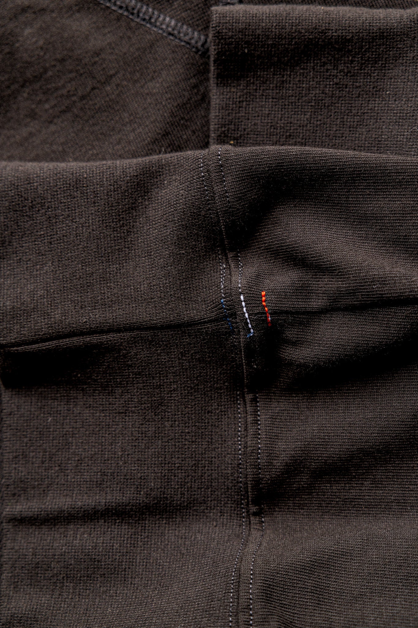 Close-up of basalt rugby jersey cotton with double-stitched seams and red and blue signature stitches.