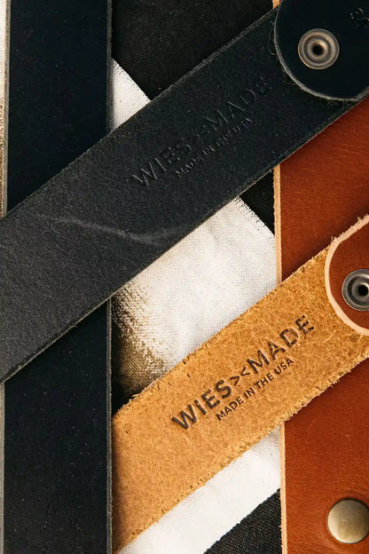 Close-up of black and saddle tan latigo leather belts stamped WiesMade, Made in the USA.