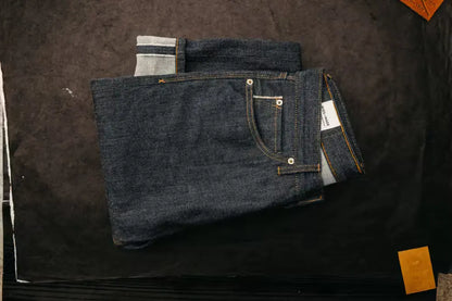 Sam Fit Jean in Raw Selvedge color with a standard fit, neatly folded on a dark textured surface, featuring visible stitching & selvedge detailing