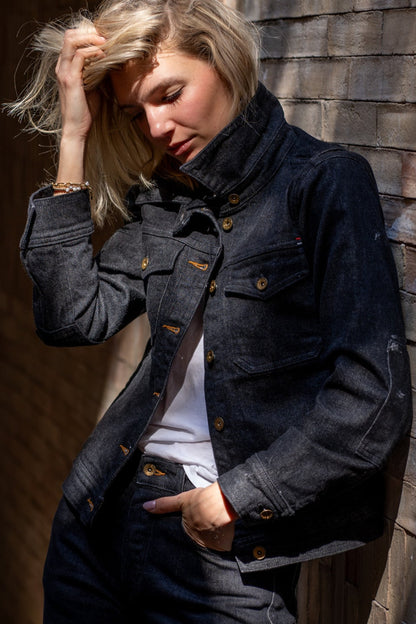 Twill denim jacket worn by a stylish woman posing against a brick wall in natural sunlight.