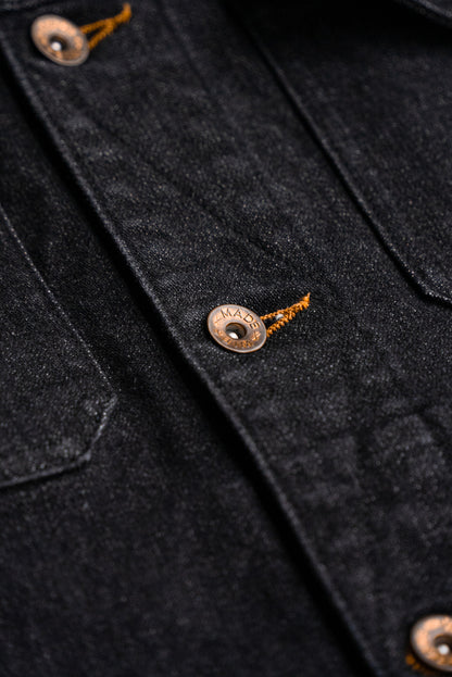 Close-up of brass WiesMade button and tobacco keyhole stitching on black denim jacket.
