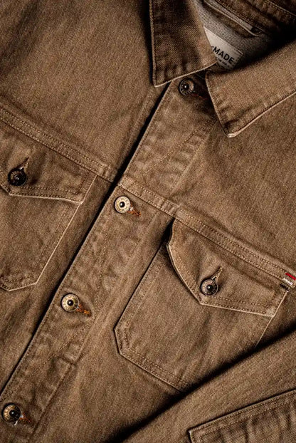 Close-up of wheat-colored broken twill denim jacket showing brass buttons, chest pockets with flaps, and flat felled seams.