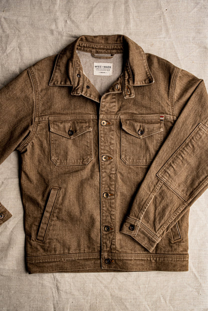 Wheat broken twill denim jacket laid flat, showing flap chest pockets, brass buttons, and welt hand pockets.