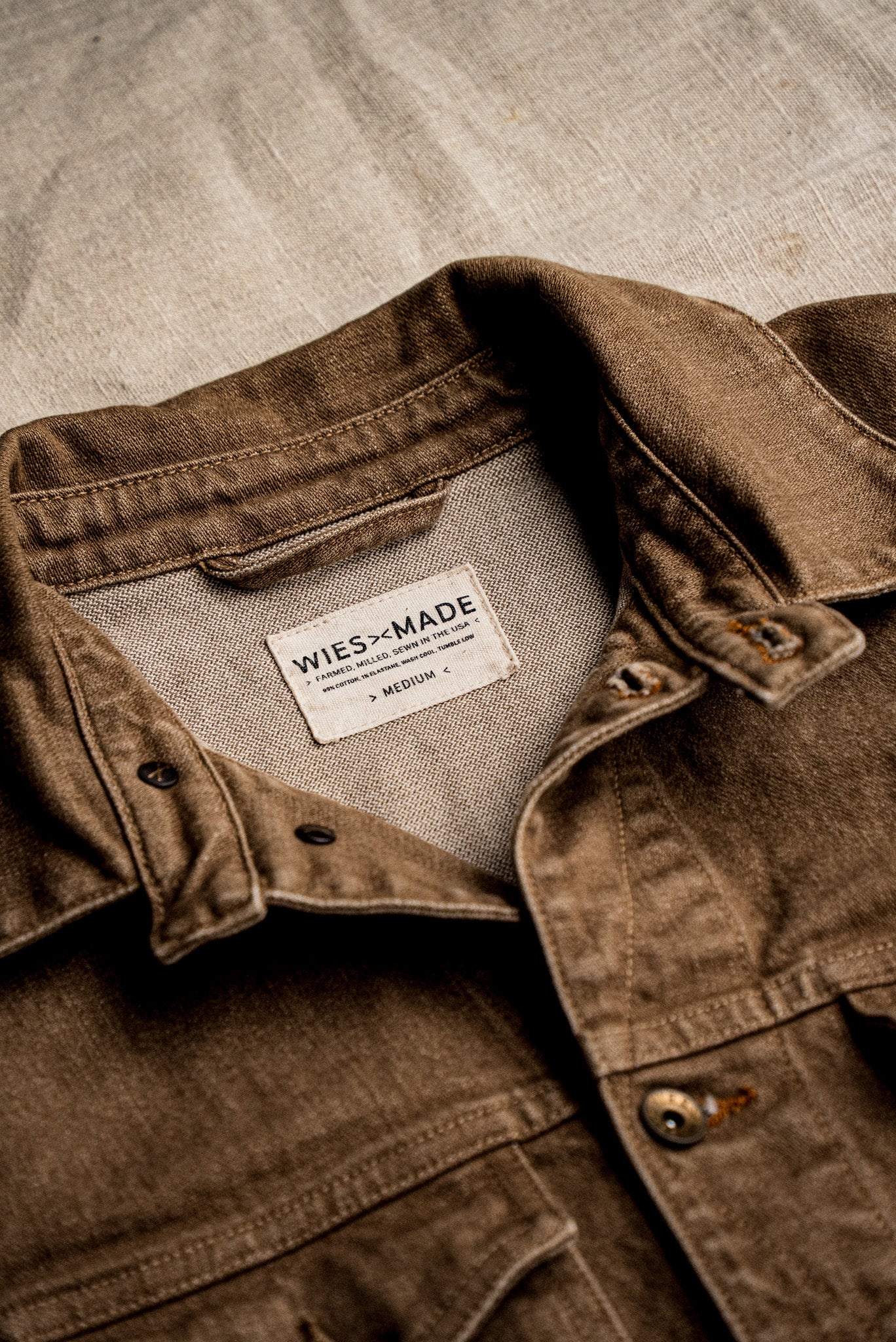 Close-up of the wheat broken twill denim jacket collar showing the WiesMade made-in-USA interior label and brass button.
