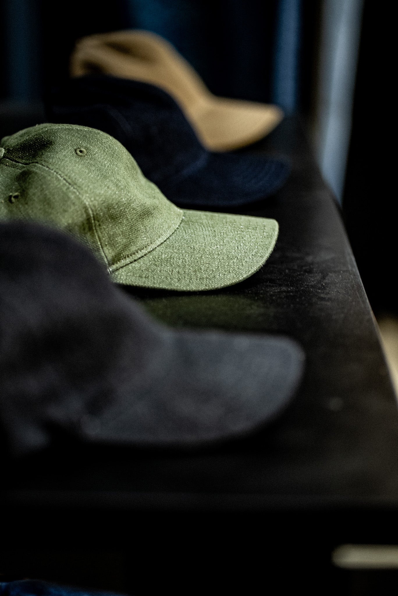 WiesMade ball cap collection displayed on a dark shelf with olive, indigo, black, and wheat colorways.