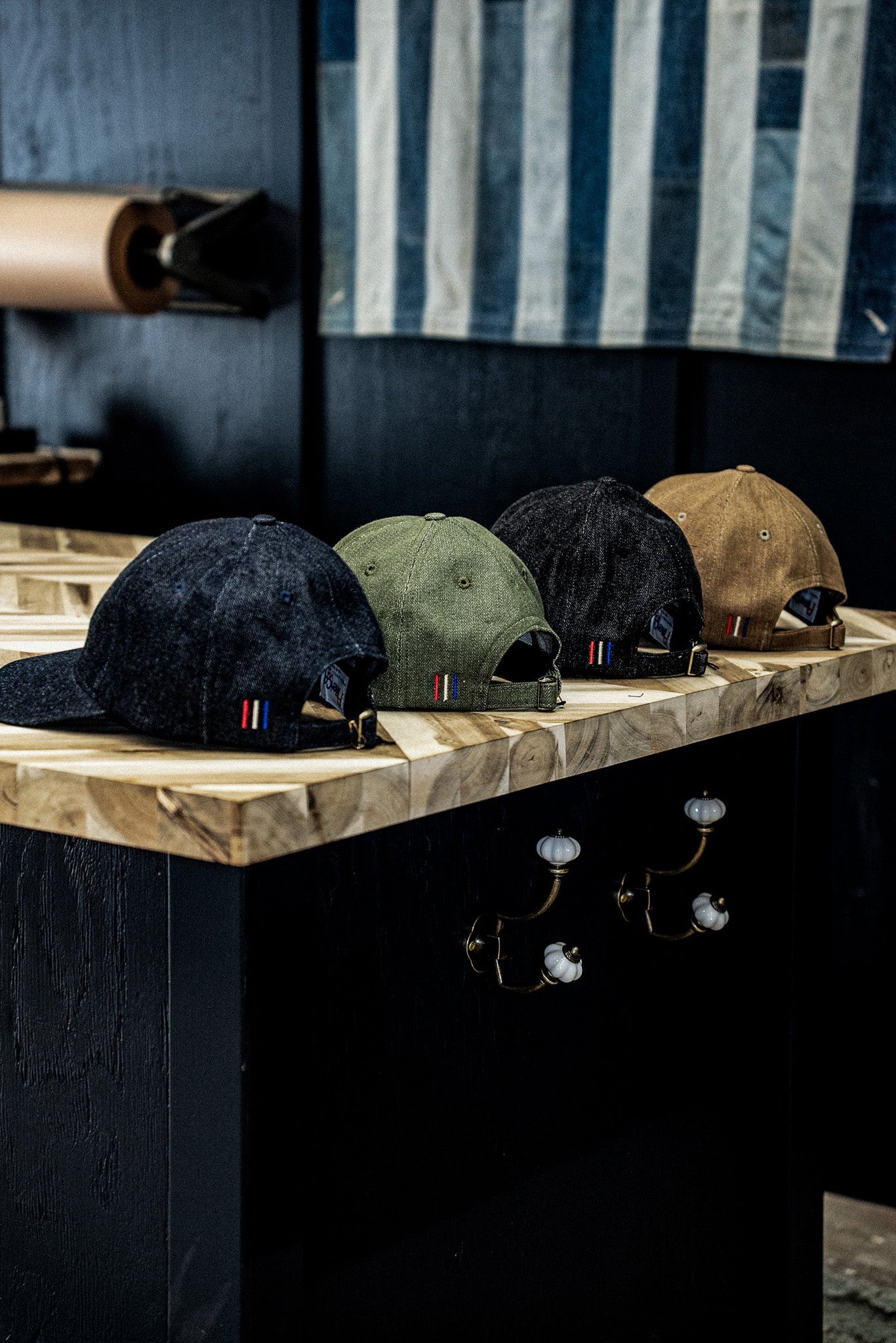 Four WiesMade ball caps in indigo, olive, black, and wheat lined up on a wooden shelf.