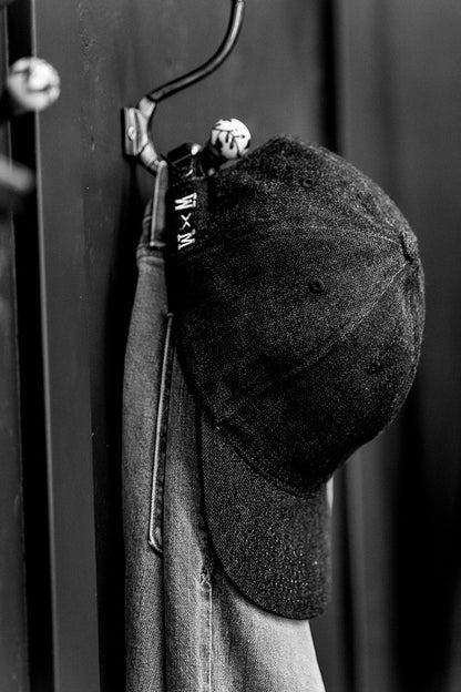 Black and white close-up of a WiesMade ball cap with W×M branded strap on a wall hook.