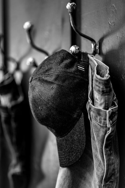 Black and white lifestyle shot of a WiesMade ball cap hanging on a wall hook with denim jeans.