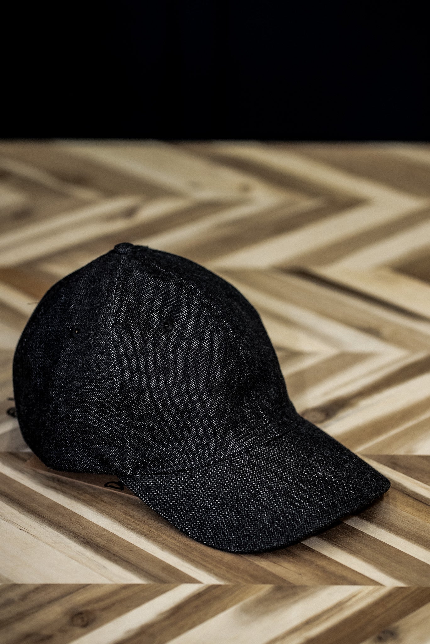 WiesMade black denim ball cap front view resting on a herringbone wood surface.