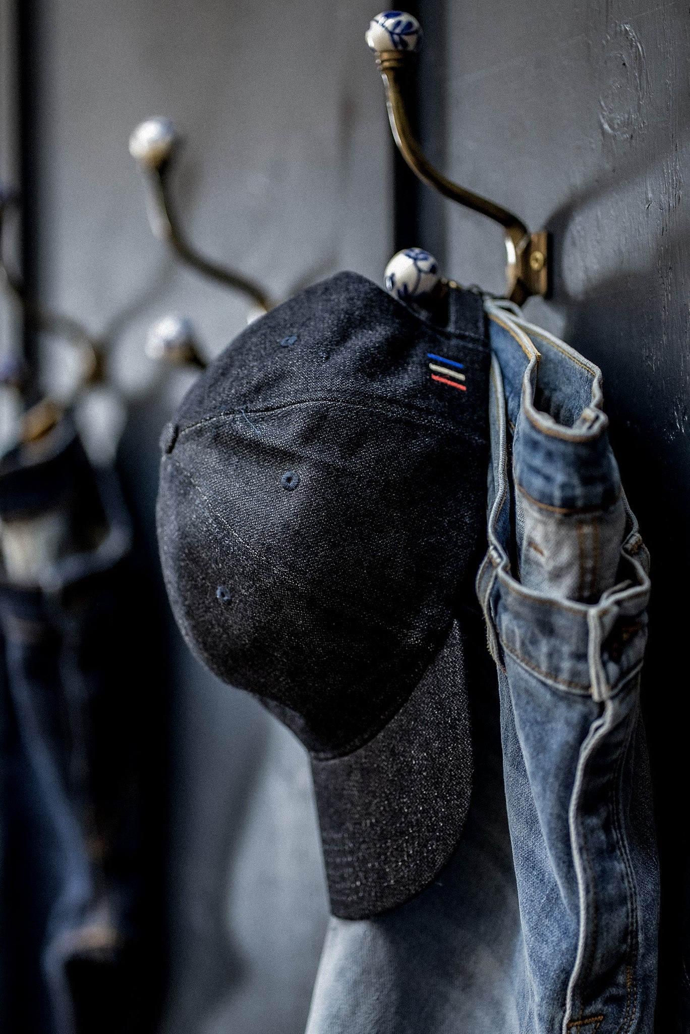 WiesMade indigo denim ball cap hanging on a wall hook next to faded jeans.