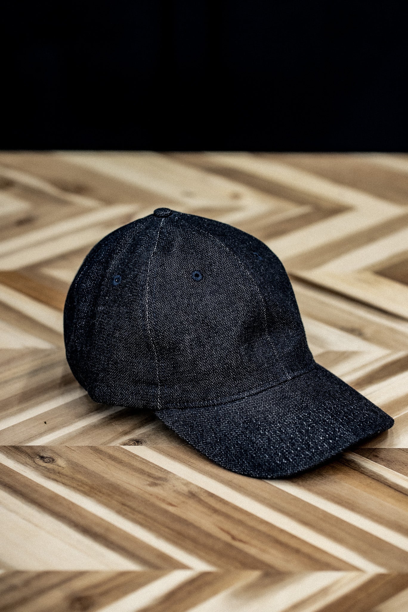 WiesMade indigo denim ball cap shown from the front on a herringbone wood surface.