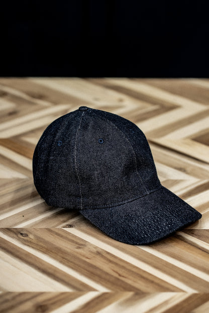 WiesMade indigo denim ball cap shown from the front on a herringbone wood surface.