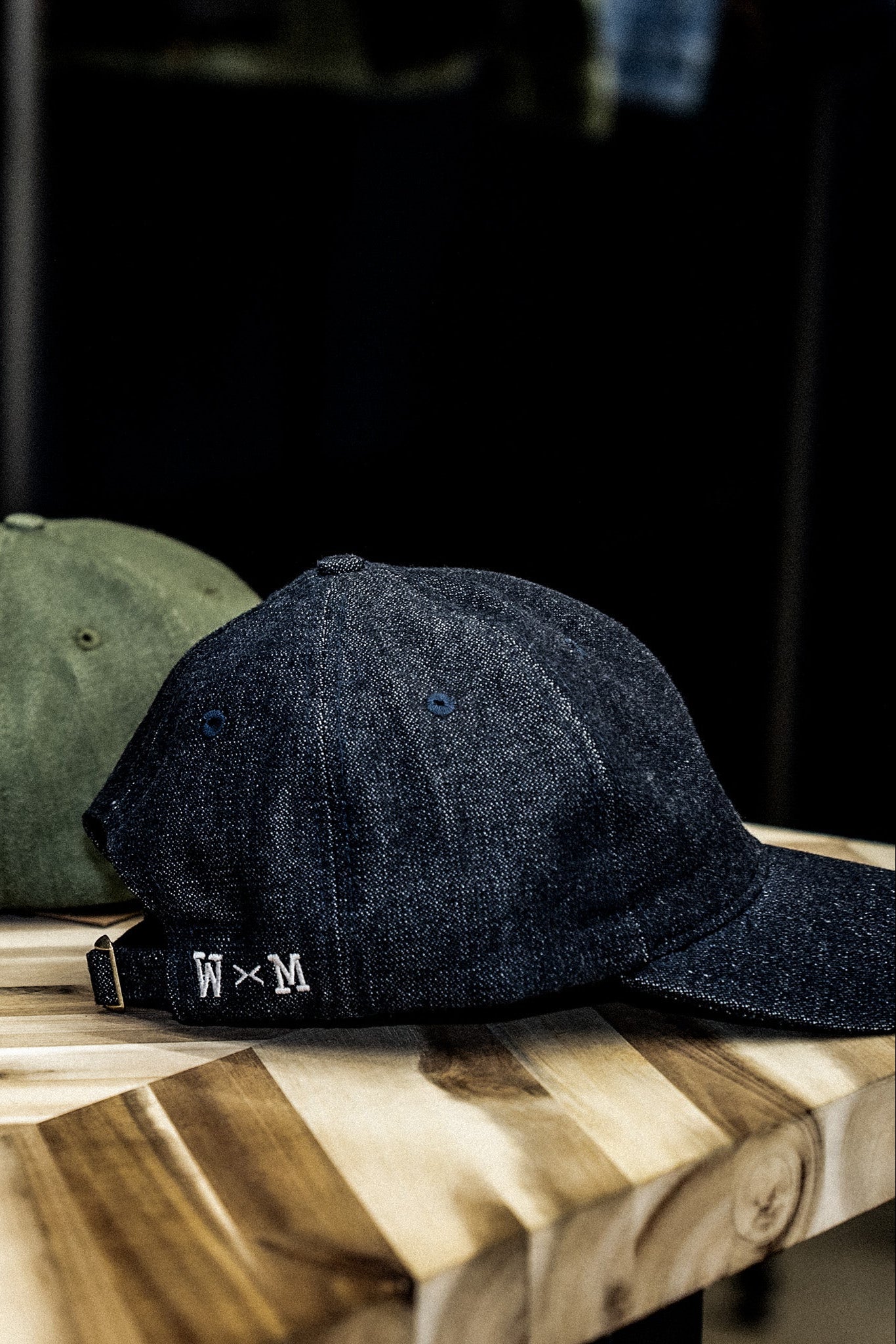 WiesMade indigo denim ball cap with branded leather strap displayed on a wooden board.