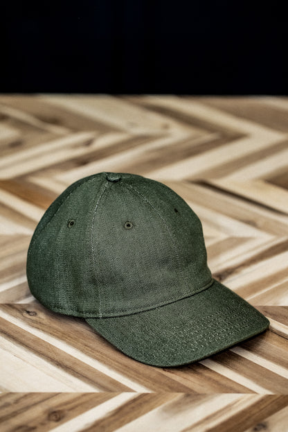 WiesMade olive green ball cap front view on a herringbone wood surface.