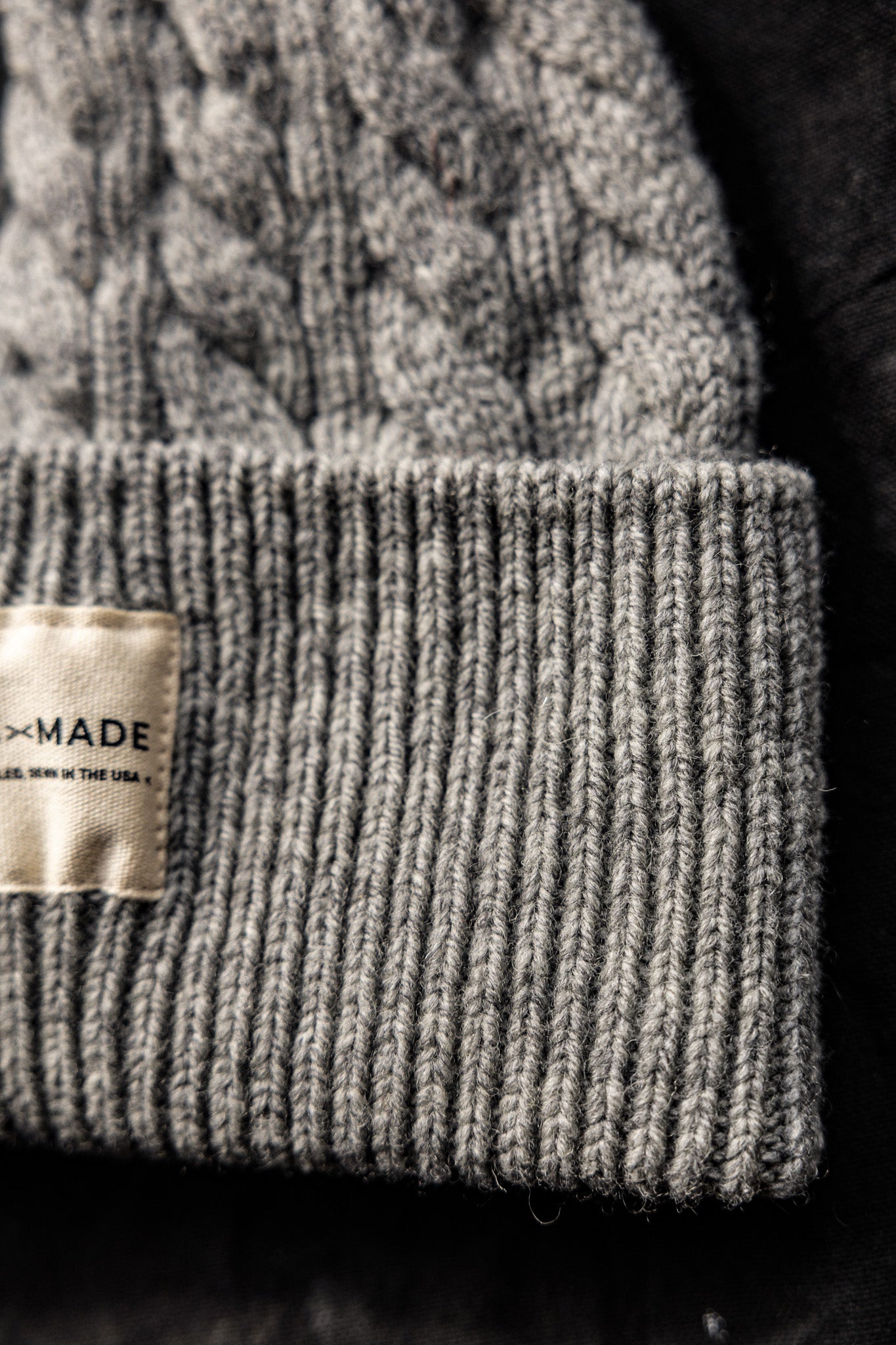 Close-up of heather gray cable-knit wool beanie with ribbed cuff and Made in the USA label.