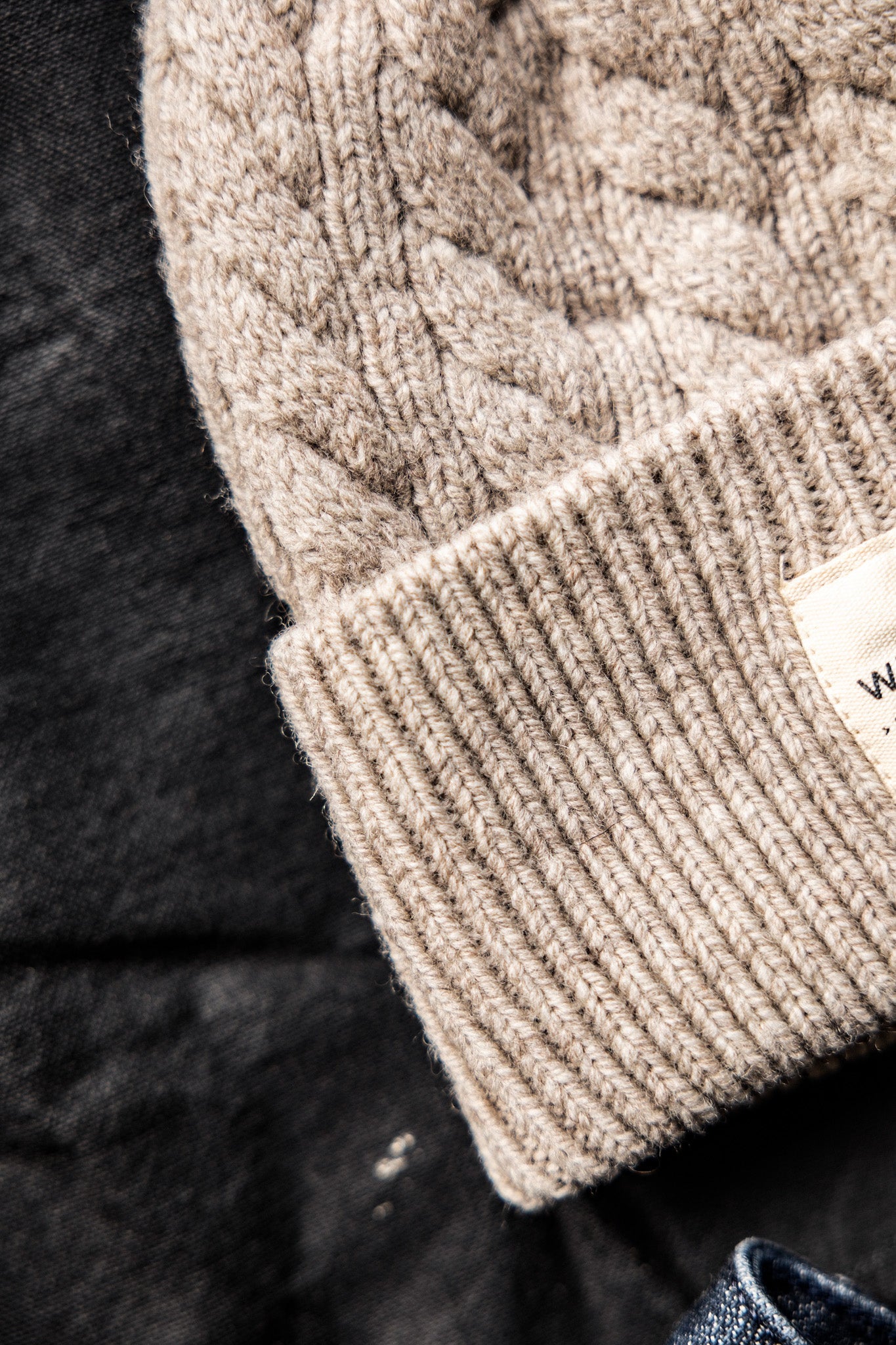 Close-up of natural cable-knit wool beanie with ribbed cuff on dark denim.