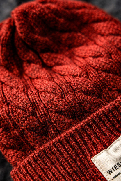 Close-up of a pomegranate red cable-knit wool beanie with a ribbed band and WiesMade label.