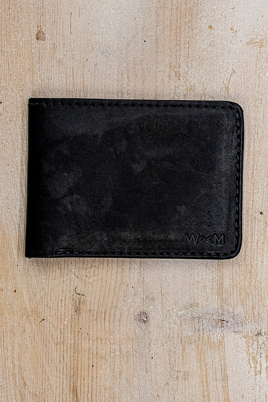 Black Horween leather bi-fold wallet with embossed WM logo on weathered wood.