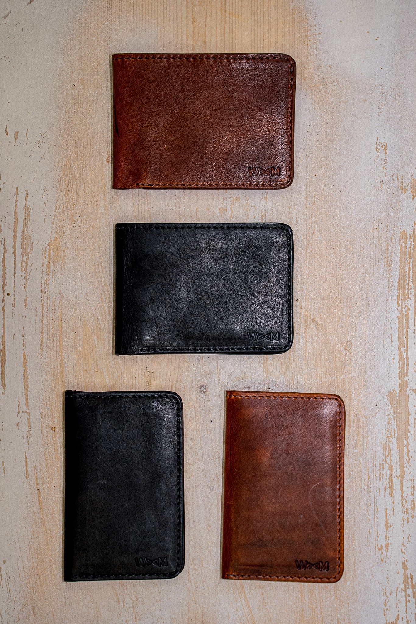 Four handmade Horween leather bifold wallets in black and brown on light wood.
