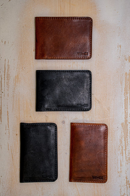 Four handmade Horween leather bifold wallets in black and brown on light wood.