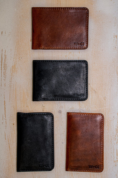 Horween leather bi-fold wallets in tan and black arranged on a weathered wood surface.