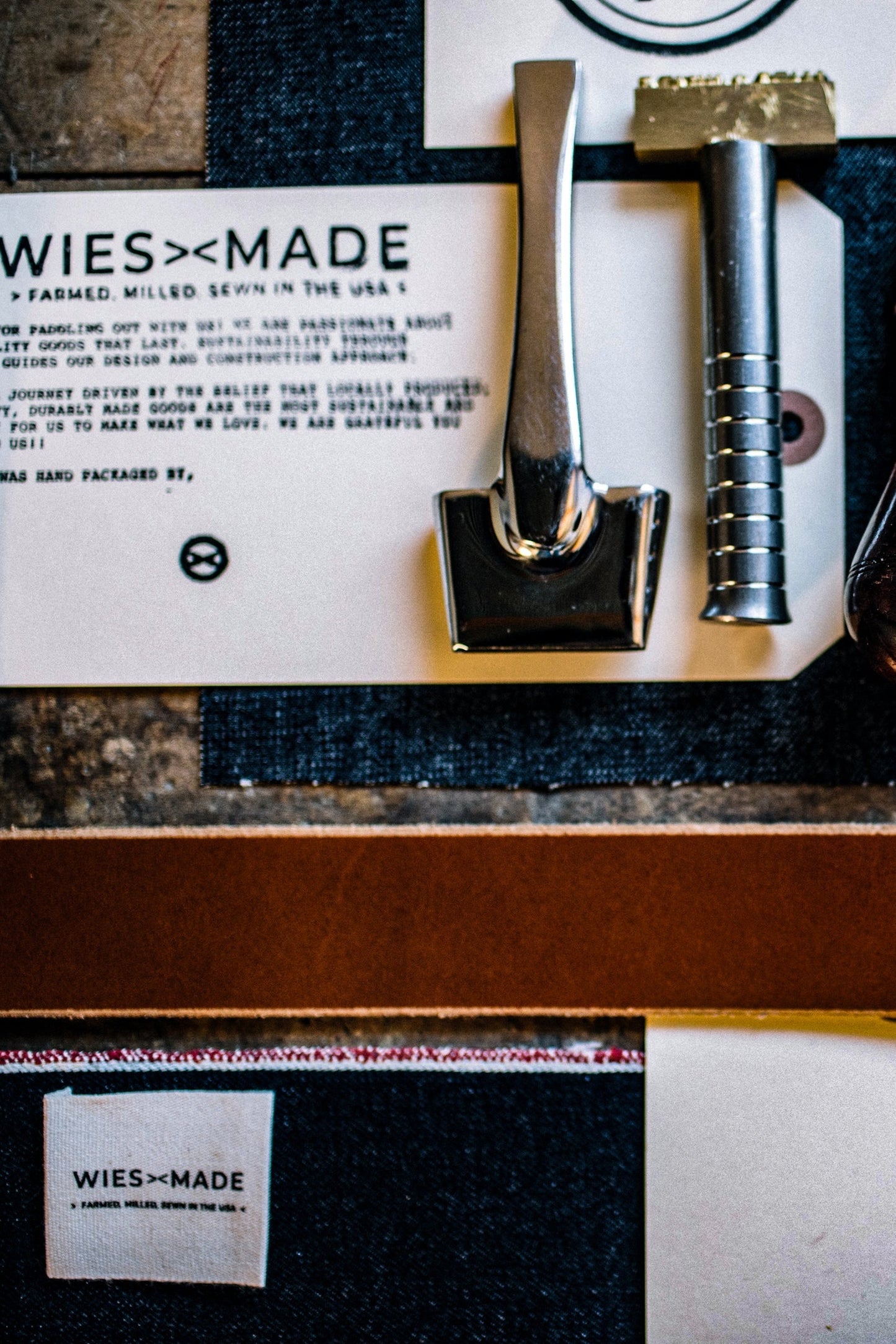 Tan Horween leather wallet stock and hand stamping tools on selvedge denim beside a WiesMade card.