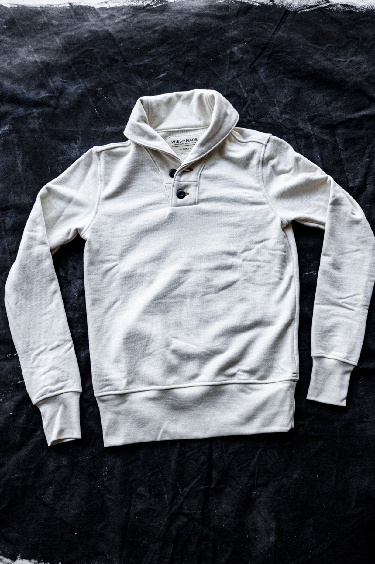 Natural French terry shawl collar pullover with two-button placket, laid flat on a dark canvas.
