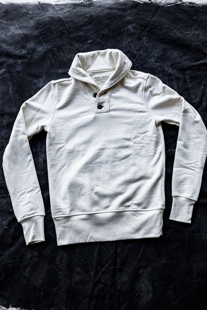 Natural French terry shawl collar pullover with two-button placket, laid flat on a dark canvas.