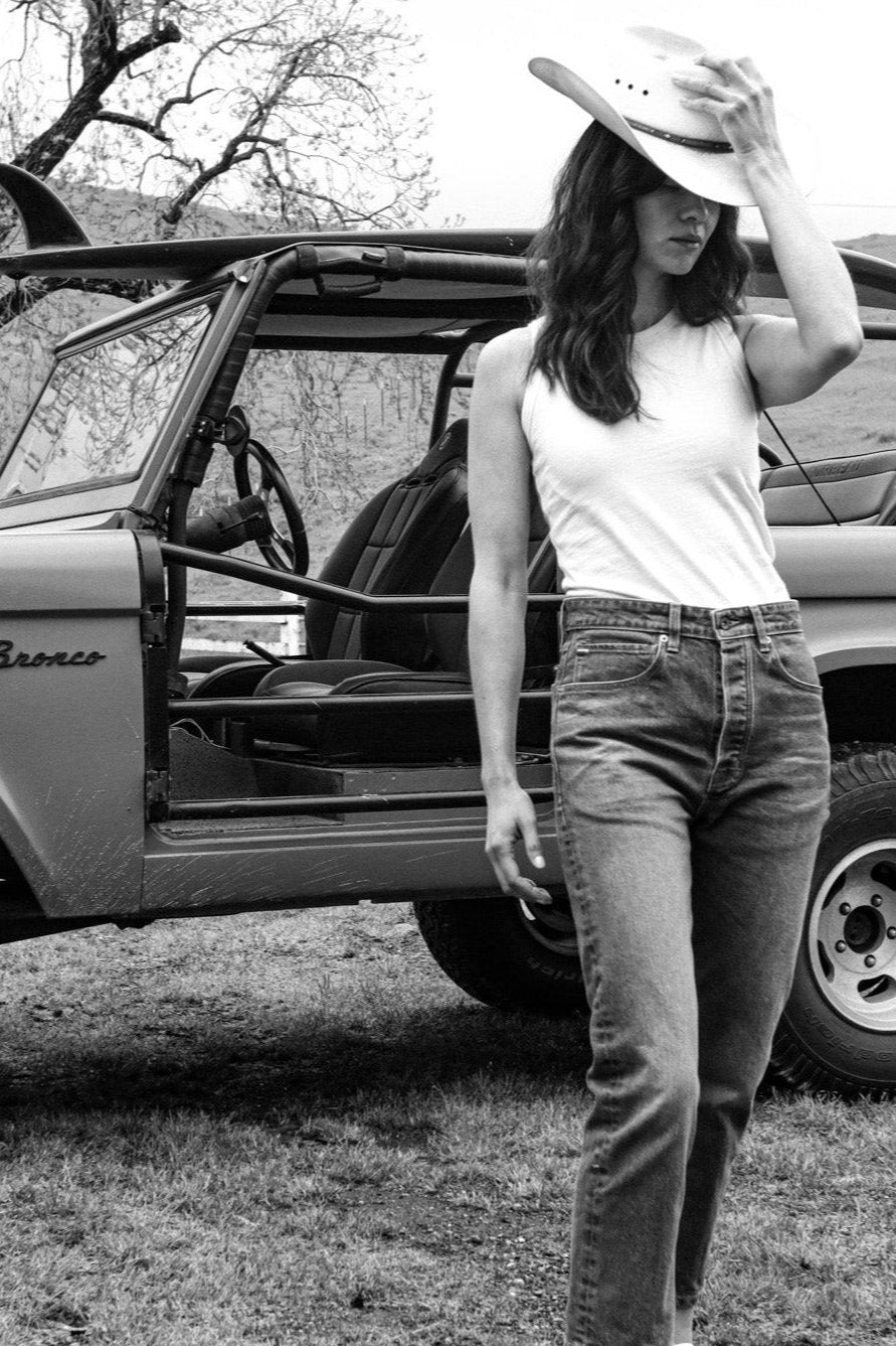 Woman in natural cotton Reyes tank and denim jeans, wearing a cowboy hat beside a vintage Bronco.