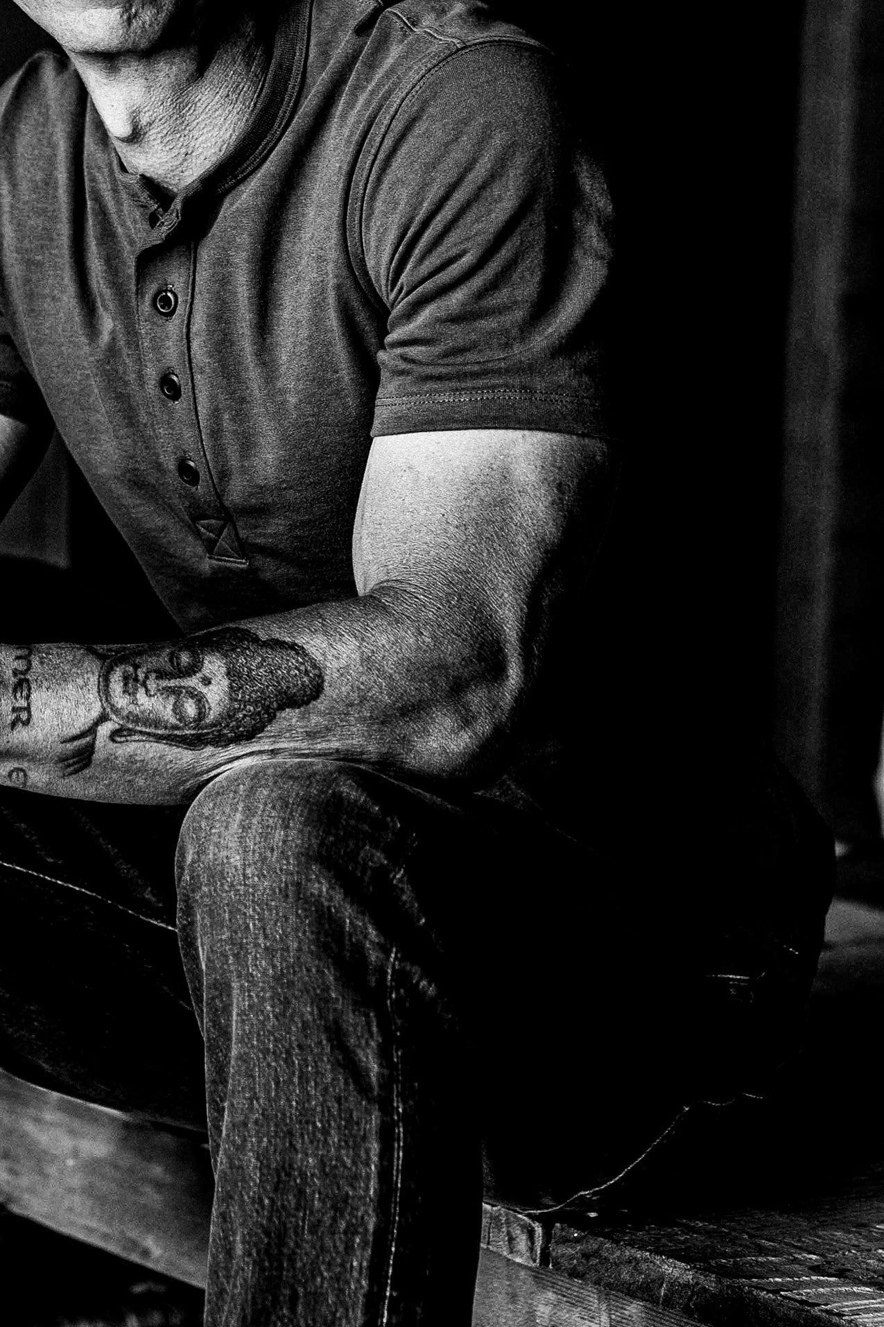 Seated model wearing the short-sleeve Bolinas four-button Henley with denim jeans, shown in black and white.