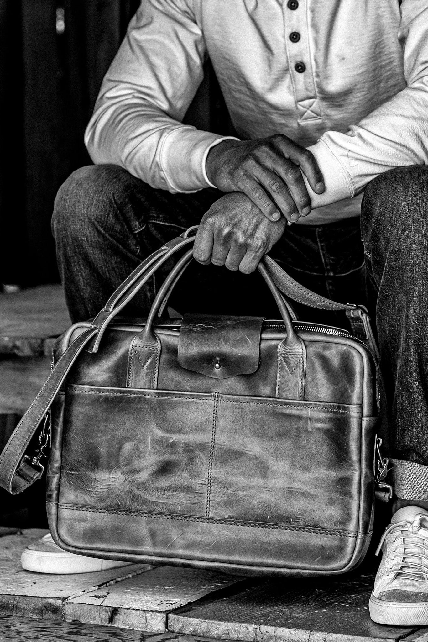 Person holding a Horween leather briefcase with dual handles, front pocket, and brass zipper.