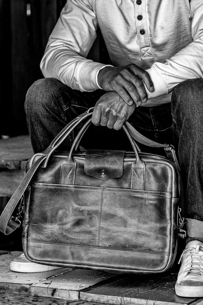 Person holding a Horween leather briefcase with dual handles, front pocket, and brass zipper.