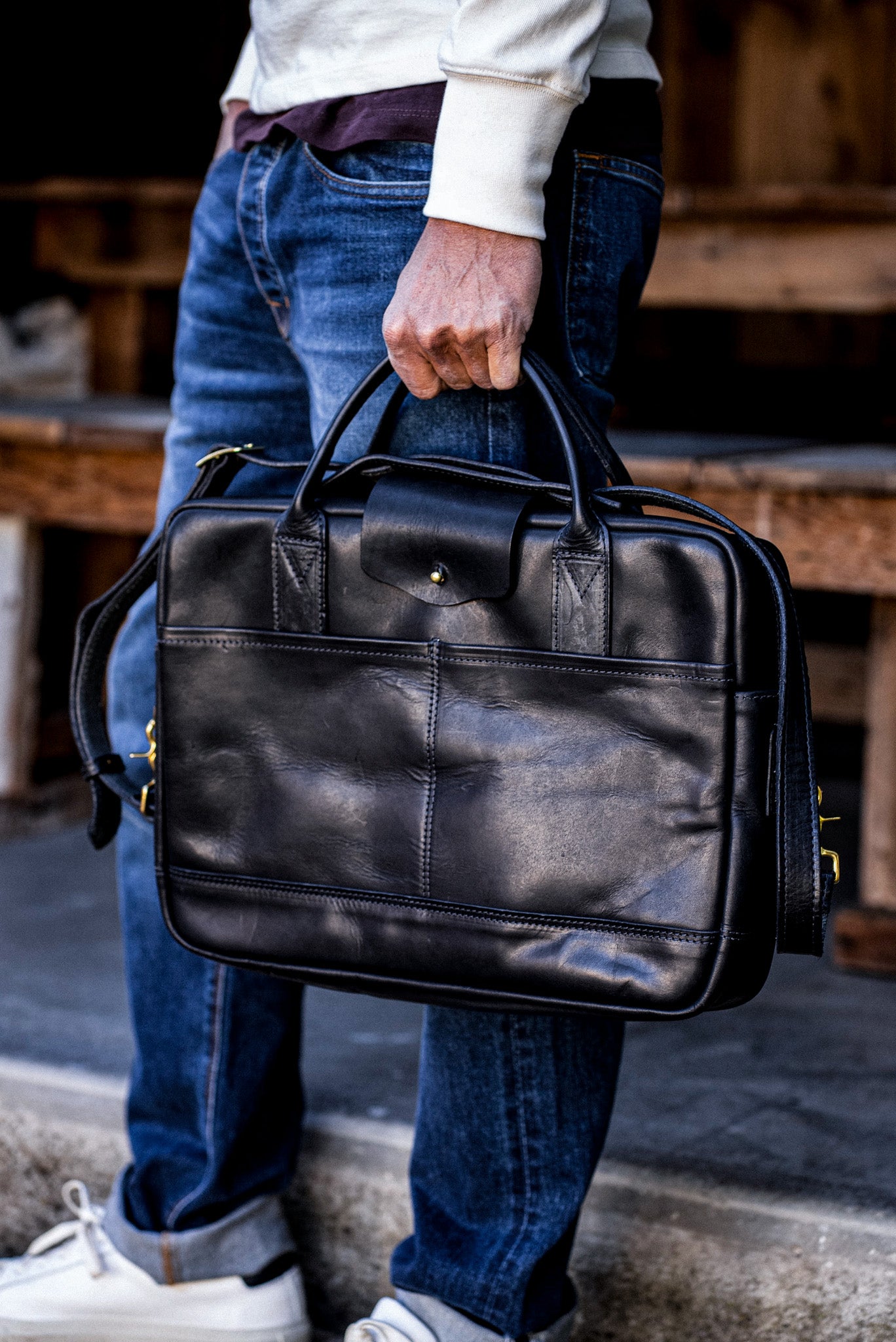 Black Horween leather briefcase with brass zipper, carried by hand over dark denim jeans.