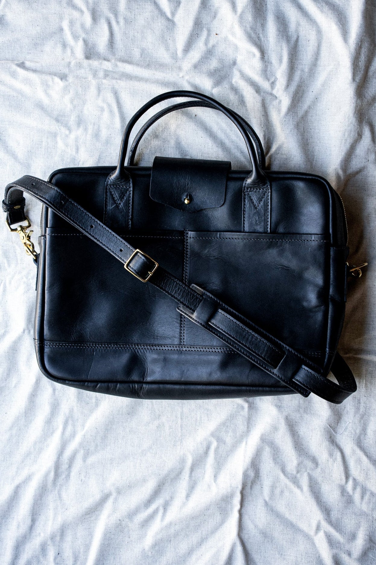 Black Horween leather briefcase with brass zipper and adjustable shoulder strap on canvas.