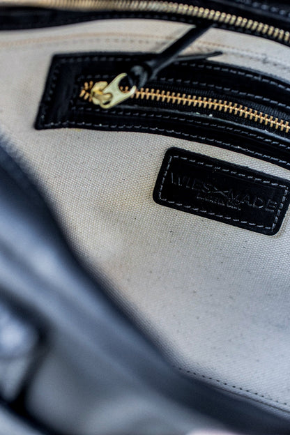 Interior of a black Horween leather brief with natural canvas lining, brass zipper, and stamped WiesMade label.