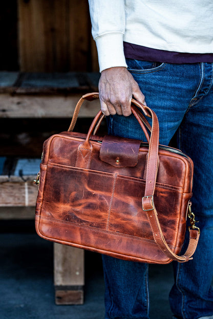 Tan Horween leather briefcase with brass hardware, carried by its top handle.