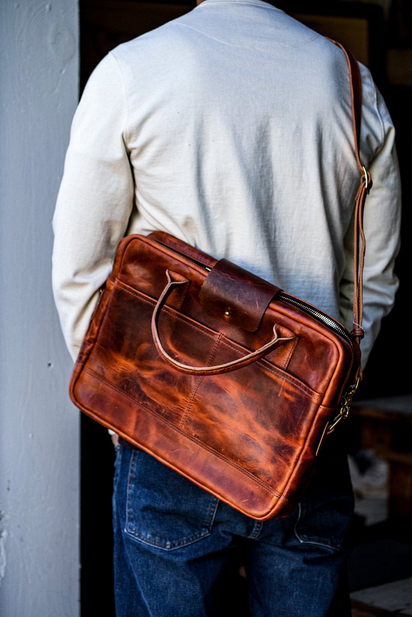 Tan Horween leather briefcase worn crossbody over the shoulder with a brass zipper.