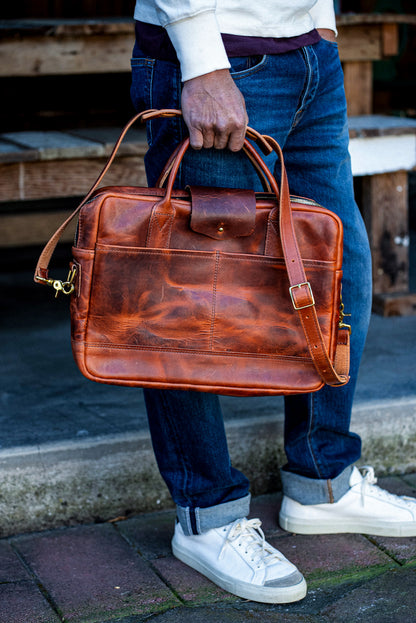 Tan Horween leather briefcase with brass hardware and shoulder strap held at a person's side.