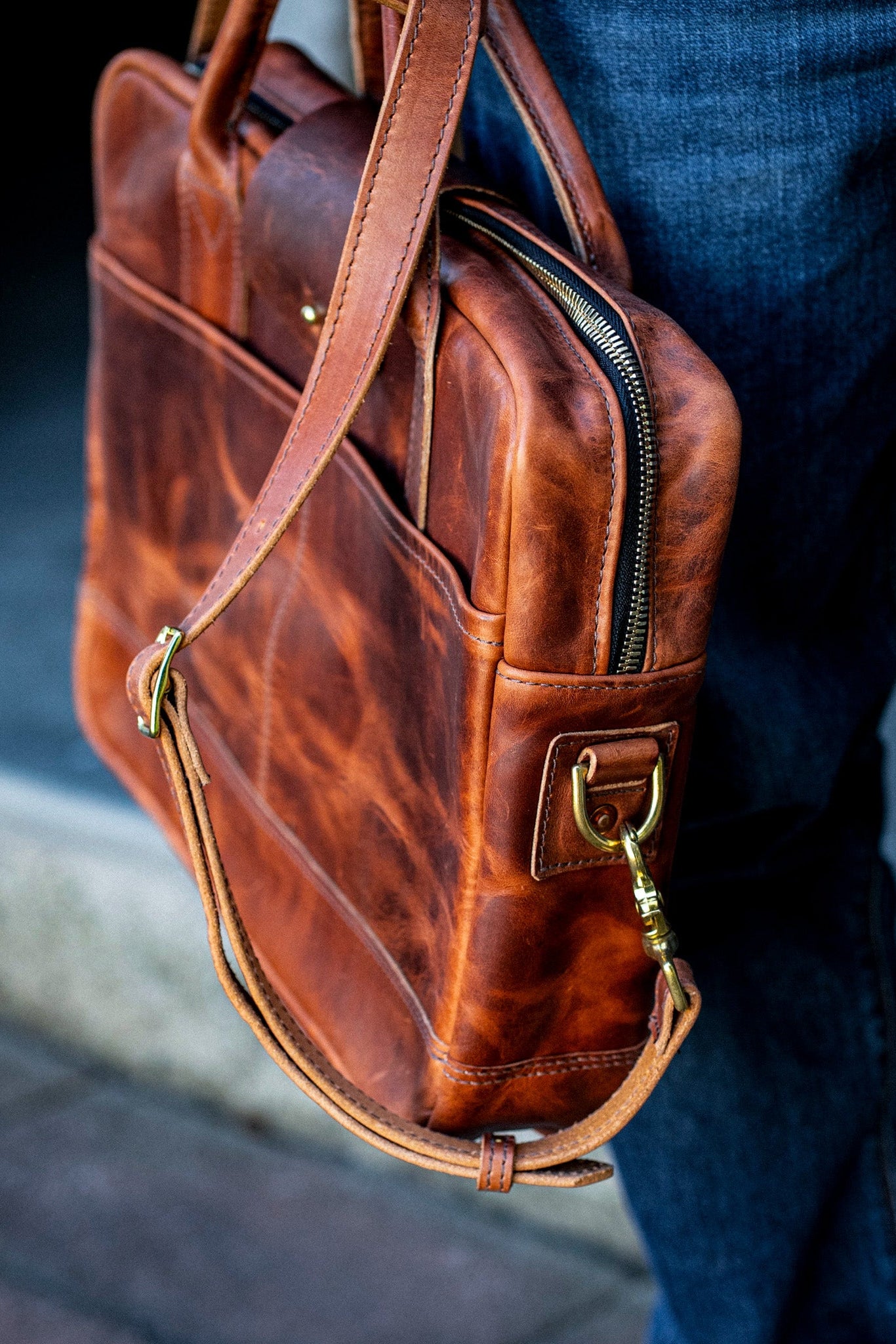 Tan Horween leather briefcase with brass zipper and shoulder strap carried against denim jeans.