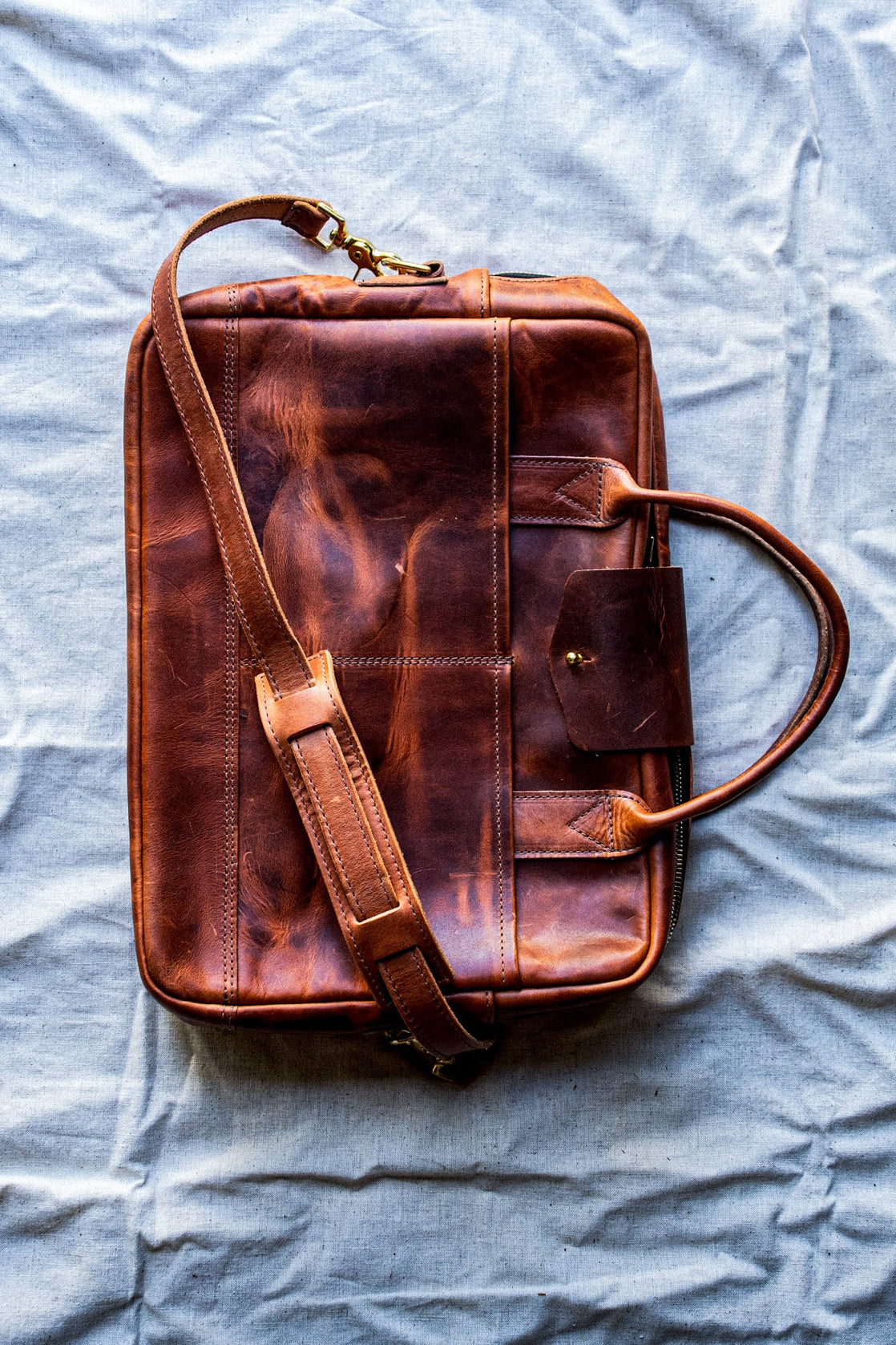 Tan Horween leather briefcase with brass zipper and adjustable shoulder strap on canvas cloth.