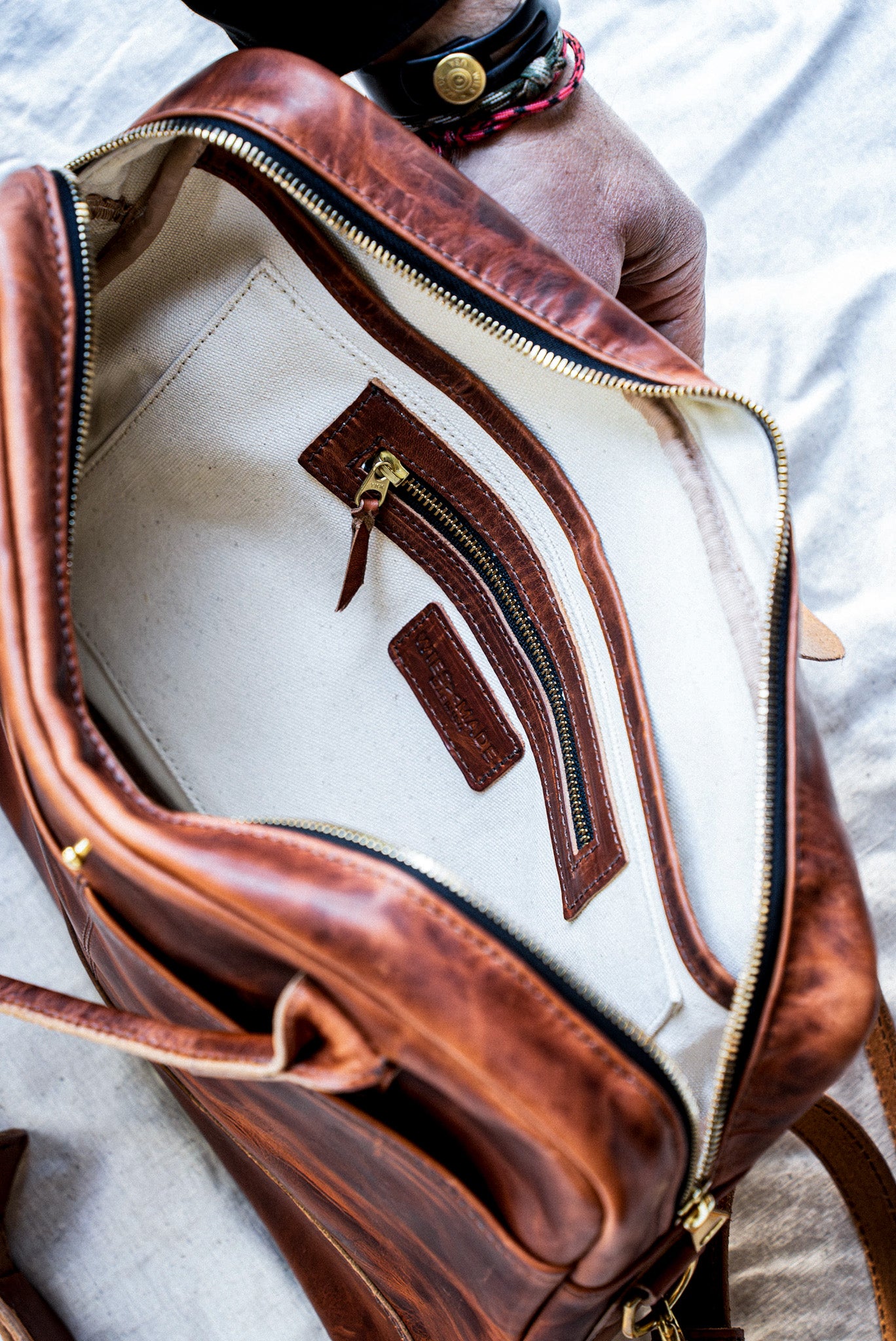 Interior of tan Horween leather briefcase with natural canvas lining and brass zip pocket.